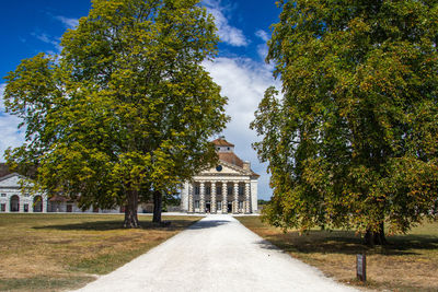 Footpath amidst trees and buildings against sky