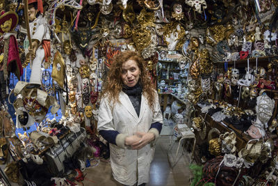 Portrait of woman smiling while standing amidst masks in store