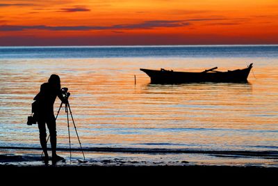 Silhouette man photographing at sea against sky during sunset