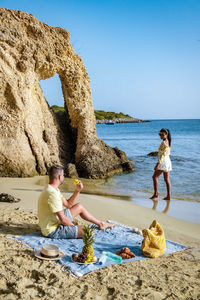 Men sitting on rock at beach against sky