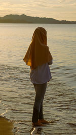 Rear view of woman standing on beach during sunset