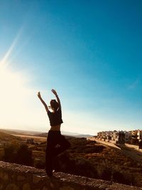 Woman standing with arms raised against sky