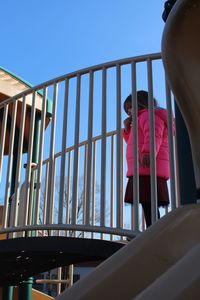 Low angle view of child on railing against clear sky