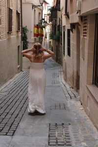 Rear view of woman standing on footpath amidst buildings