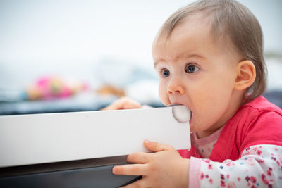 Cute baby girl biting table while sitting at home