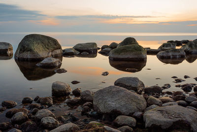 Rocks by sea against sky during sunset