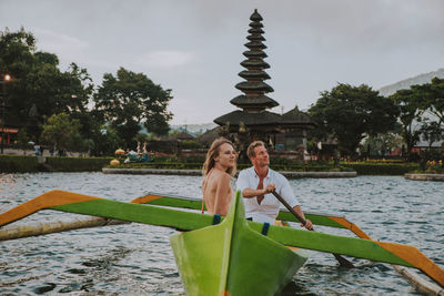 Couple in outrigger boat on lake against temple
