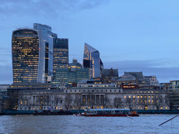 Modern buildings in city of london by river thames against sky at dusk
