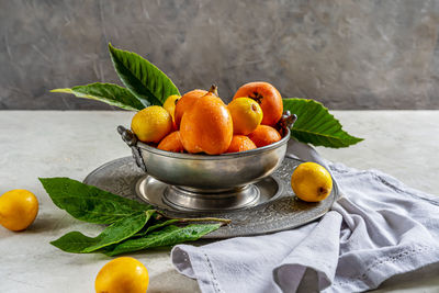 Medlar fruits on antique tin bowl and plate with leaves over concrete background, grey napkin.