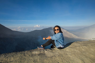 Young woman sitting on land against sky