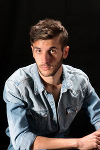 Portrait of young man sitting against black background