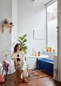 Portrait of woman seated in corner by table, window, banquette