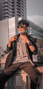 Portrait of man wearing sunglasses standing against buildings in city