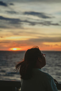 Side view of woman looking at sea against sky during sunset