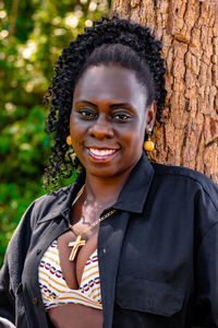 Portrait of smiling mid adult woman standing against tree trunk