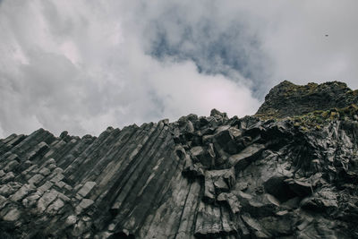 Low angle view of rocky mountain against cloudy sky