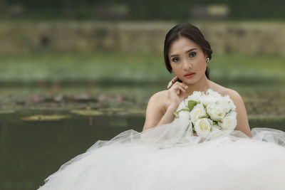 Portrait of beautiful bride holding white roses bouquet against lake