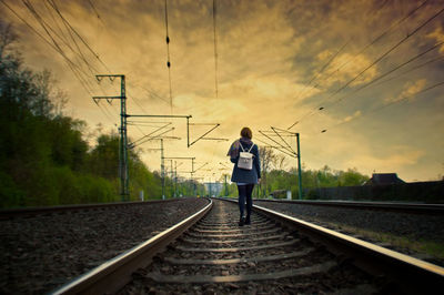 Rear view of woman walking on railroad track during sunset