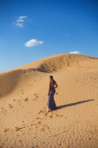 Brunette woman in a long leopard dress stands with her back in the desert at sunset. go everywhere