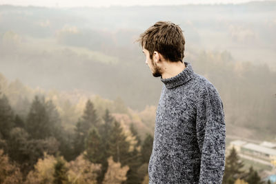 Man looking at view while standing on cliff during foggy weather