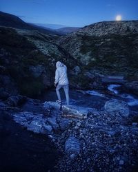 Rear view of man standing on rock against sky
