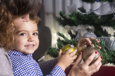 Portrait of happy boy with mother decorating christmas tree at home