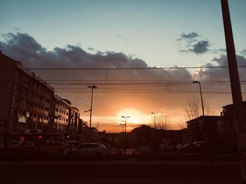 Cars on street by buildings against sky at sunset