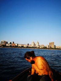 Shirtless man sitting in boat on sea against clear sky