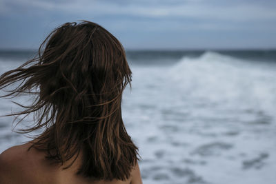 Rear view of mid adult woman standing at beach against cloudy sky