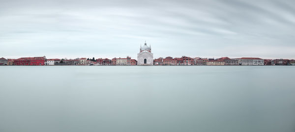 City at waterfront against cloudy sky