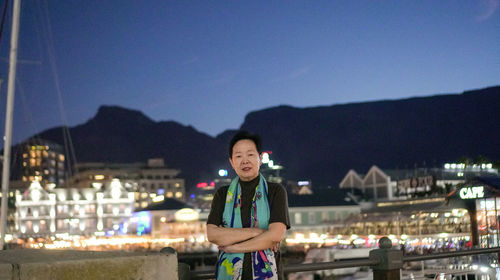 Portrait of man standing against illuminated buildings in city at night