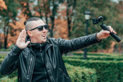 Young man wearing sunglasses filming with video camera in park