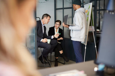 Bank managers discussing over solar toy car while businessman giving presentation in creative office