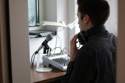 Rear view of man wearing headphones standing in recording studio