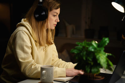 Woman listening music in headphones and using laptop at night