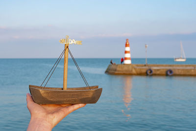 Hand of girl holding wooden boat souvenir with red and light lighthouse, nida, lithuania