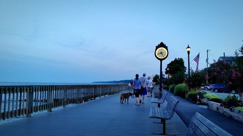 Rear view of couple with dog on boardwalk against sky