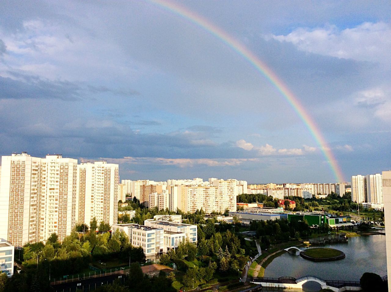 building exterior, architecture, built structure, city, sky, rainbow, cityscape, cloud - sky, tree, high angle view, road, car, cloud, cloudy, city life, transportation, residential district, skyscraper, residential building, outdoors