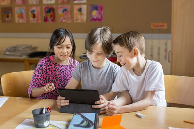 Three children looking at digital tablet in classromm