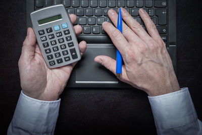 Cropped hands of businessman using calculator and laptop at desk