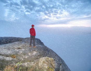 Man standing on rock by mountain against sky