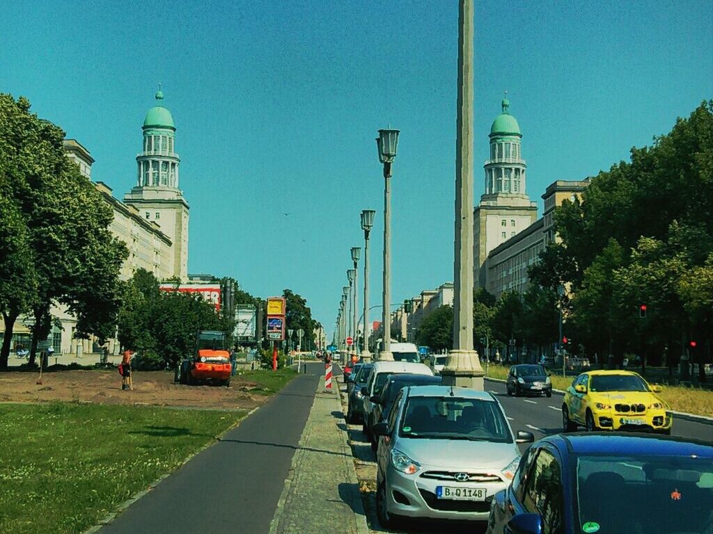 transportation, architecture, car, building exterior, built structure, land vehicle, tree, mode of transport, road, clear sky, street, blue, city, travel, tower, road marking, street light, the way forward, incidental people, on the move