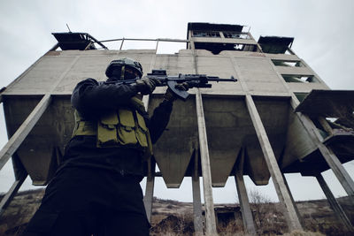 Low angle view of male soldier aiming gun while standing against built structure