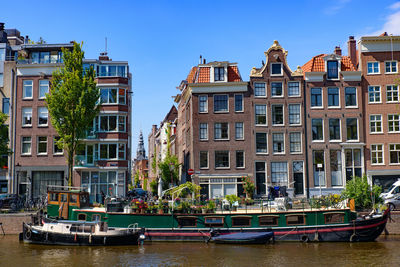 Boats moored in canal by buildings against sky