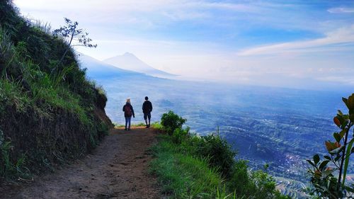 Rear view of people walking on mountain against sky