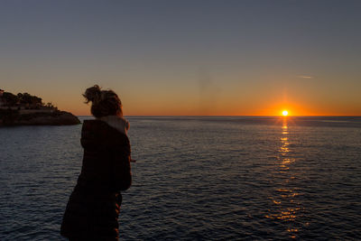 Woman looking at sea against sky during sunset