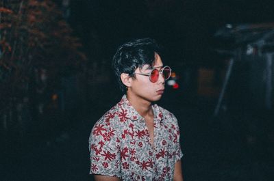 Young man looking away while standing outdoors at night