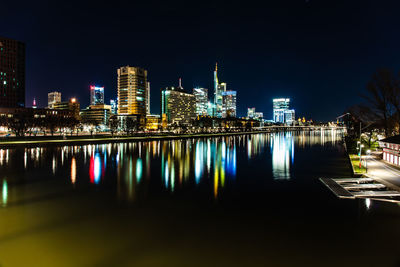 Illuminated buildings by river against sky at night