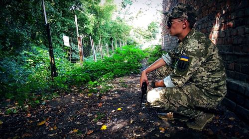 Side view of army solider crouching on field by brick wall