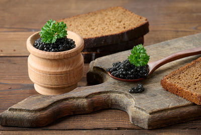 Fresh grainy black paddlefish caviar in brown wooden spoon on a brown table, close up